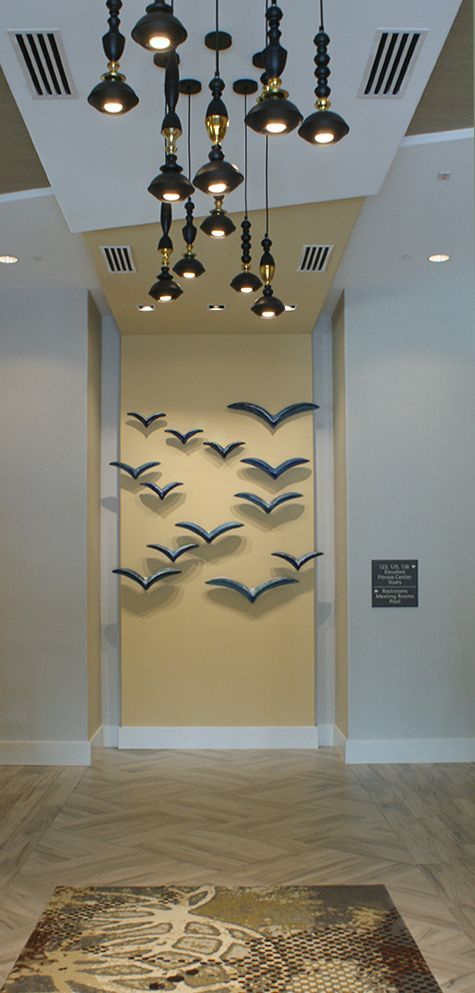 A hallway with a chandelier hanging from the ceiling and a wall with birds on it.