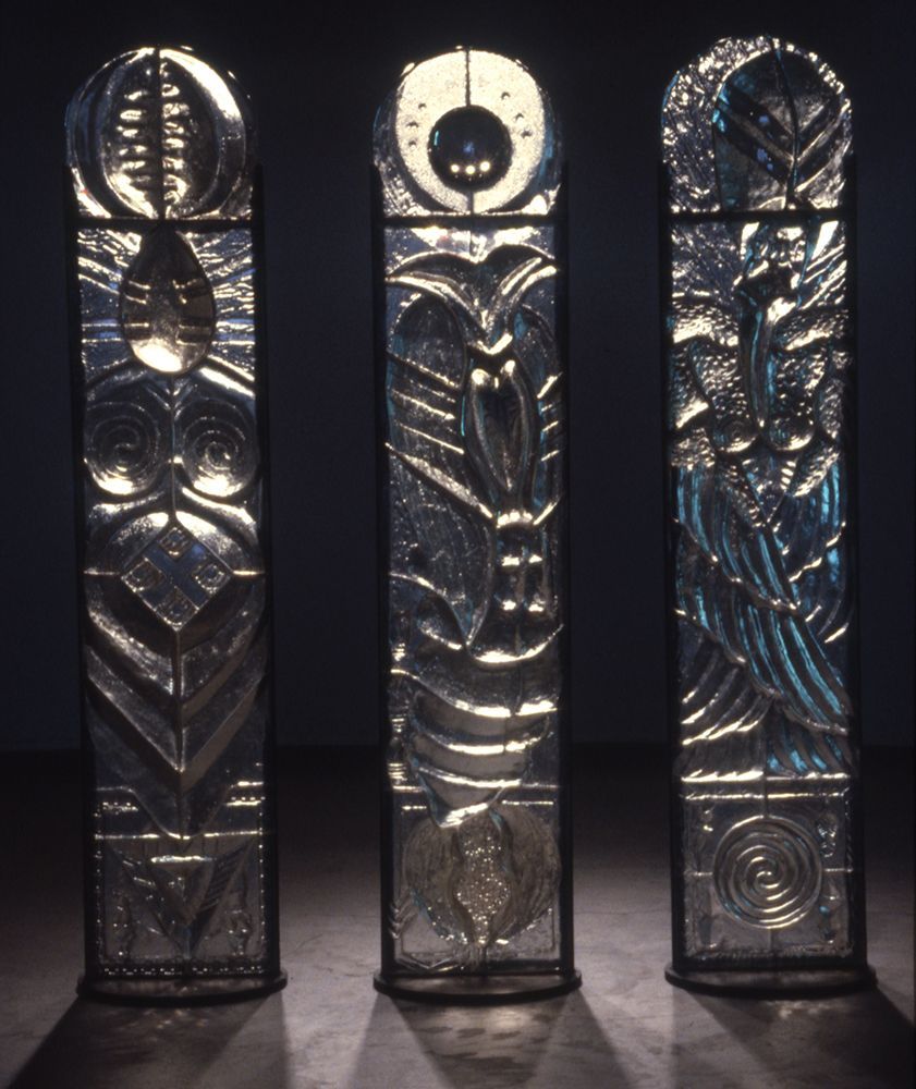 Three stained glass sculptures are lined up in a dark room