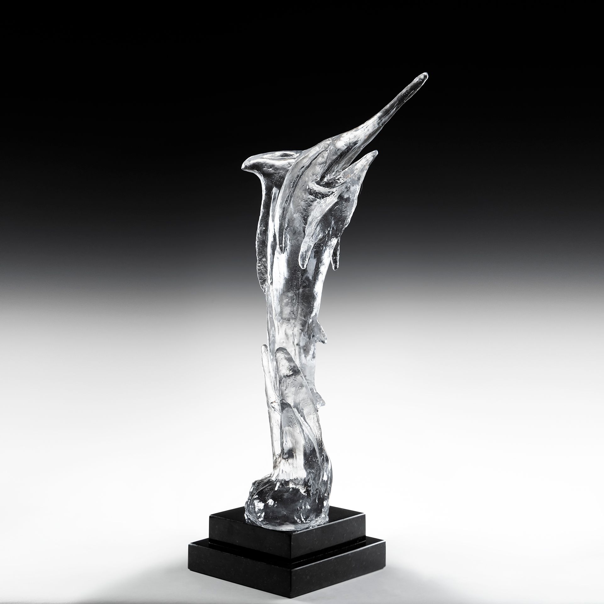 A clear glass statue of a dolphin on a black base