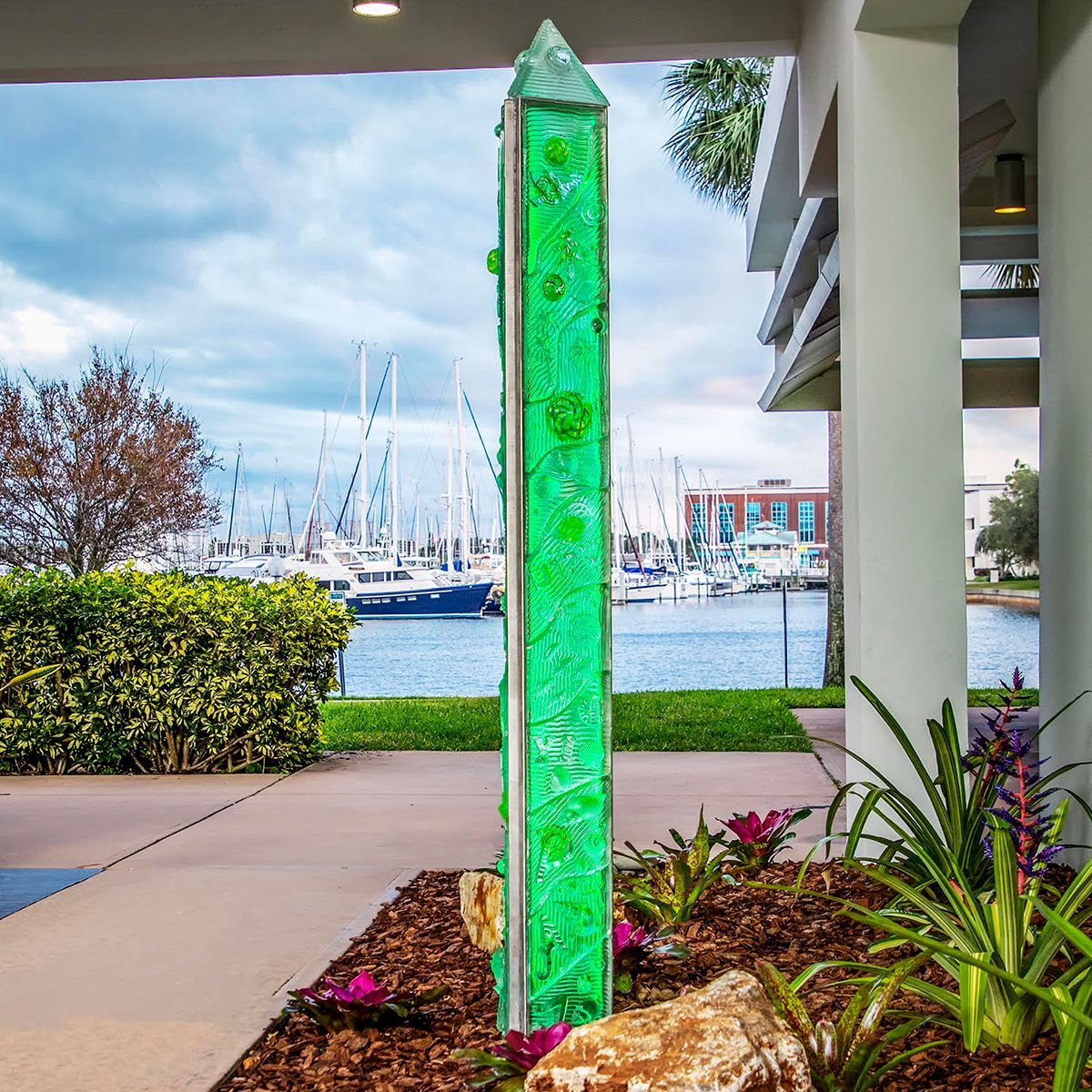 A green sculpture in a garden with boats in the background