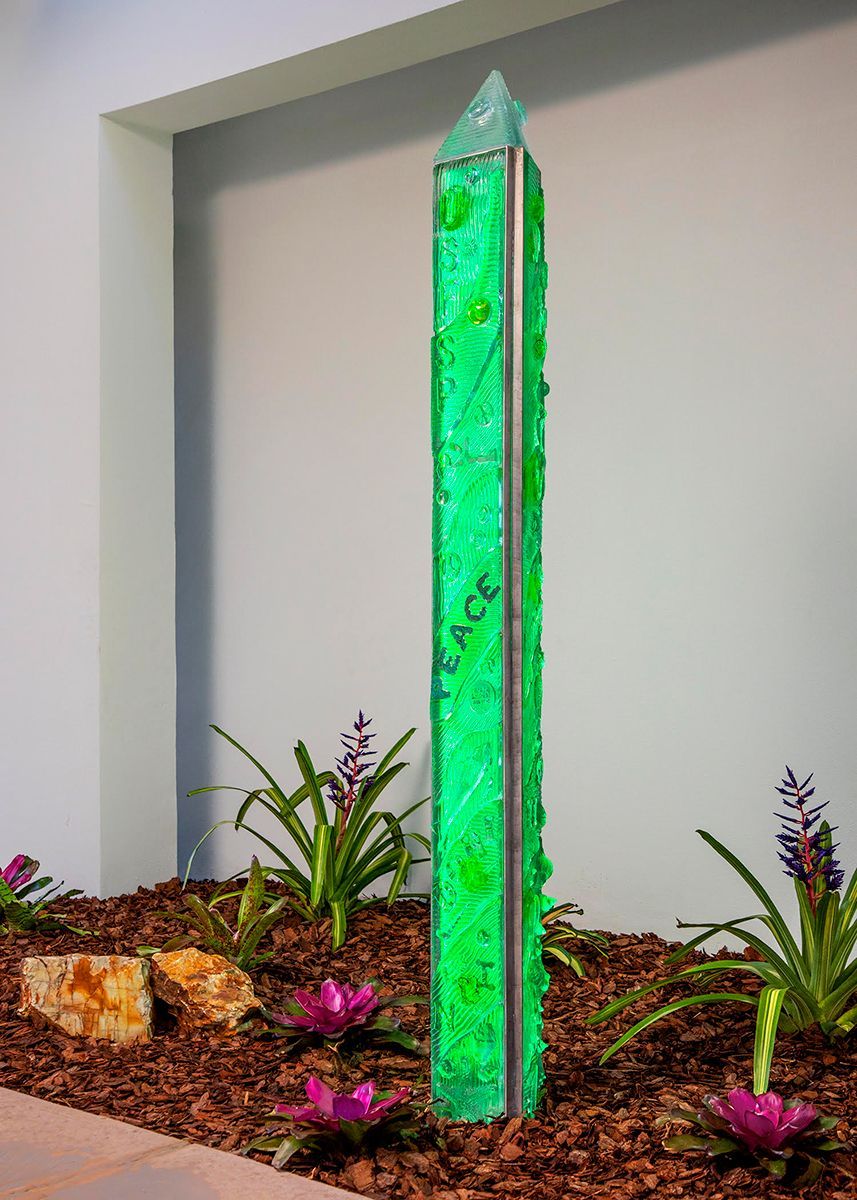A green sculpture in a garden with flowers and rocks