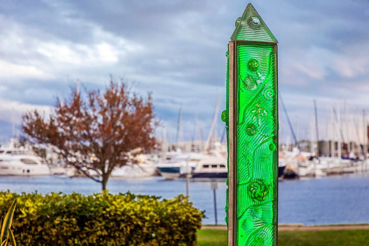 A green sculpture is sitting in front of a harbor with boats in the background.