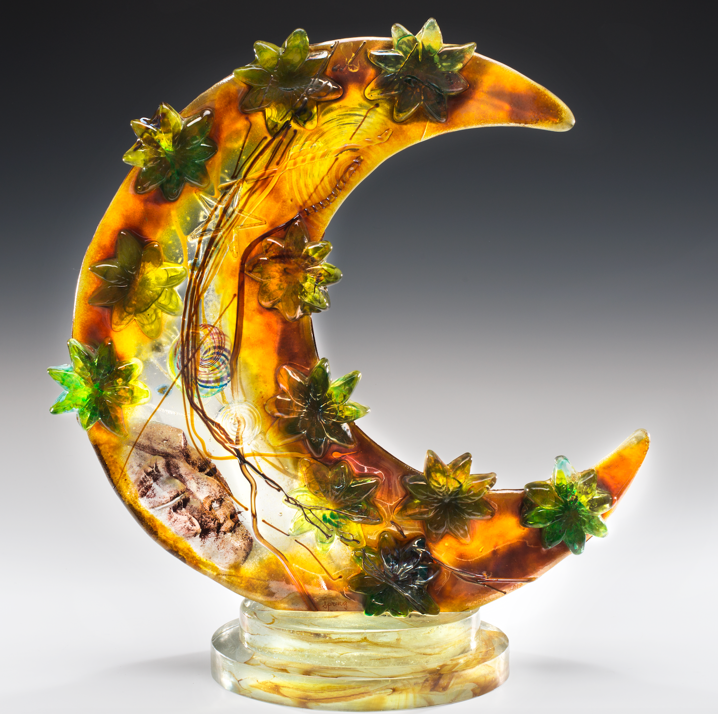 A glass sculpture of a crescent moon with leaves on it