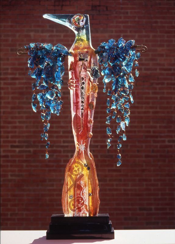 A statue of a bird with blue wings is sitting on a table in front of a brick wall
