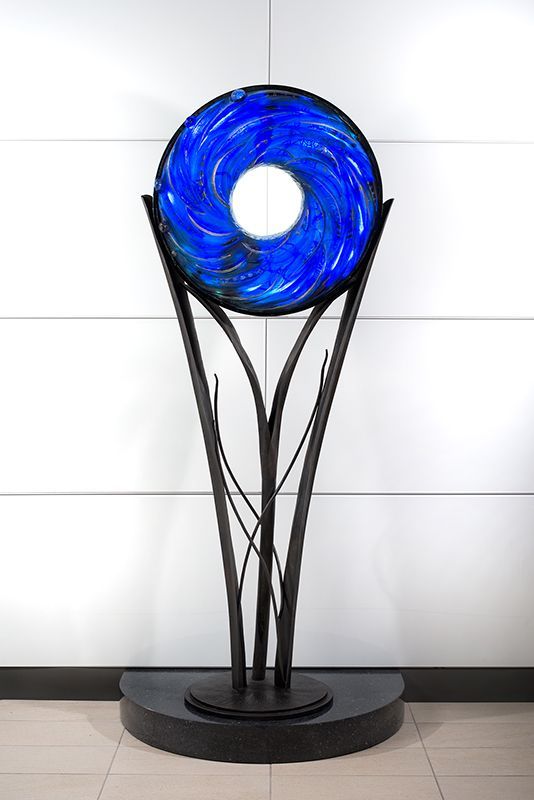 A blue glass sculpture is sitting in front of a white wall.