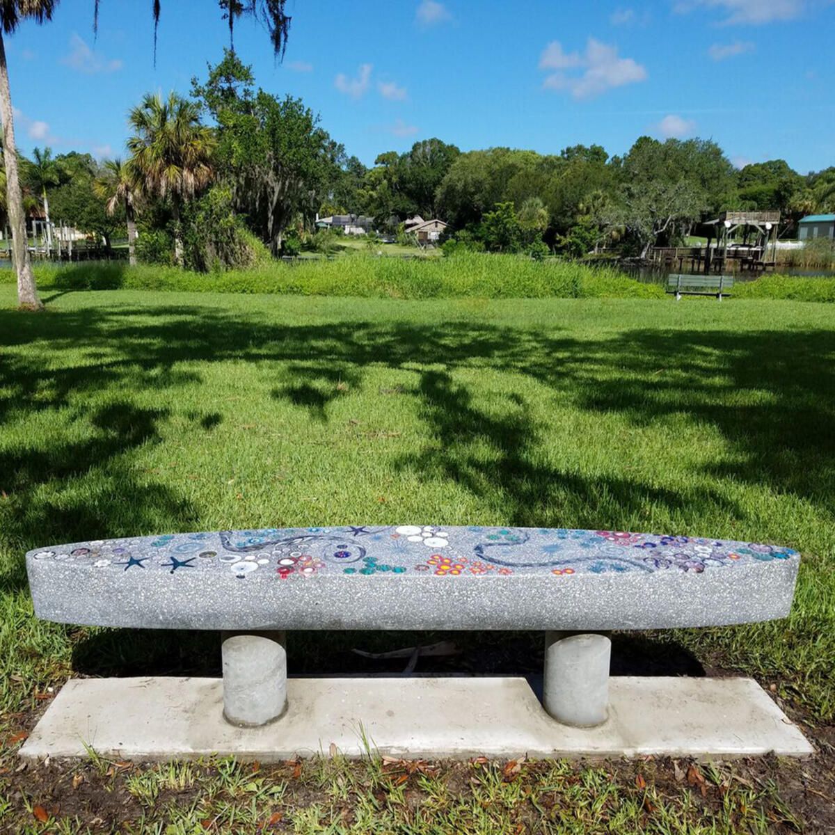 A park bench with a mosaic design sits in the middle of a grassy field