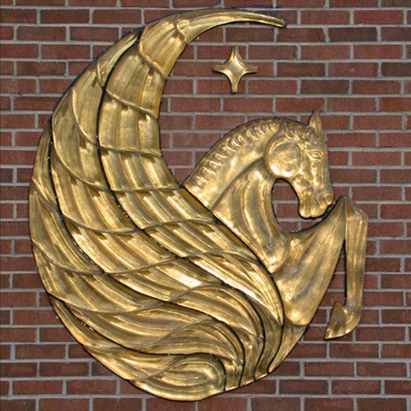 A gold statue of a horse with wings on a brick wall