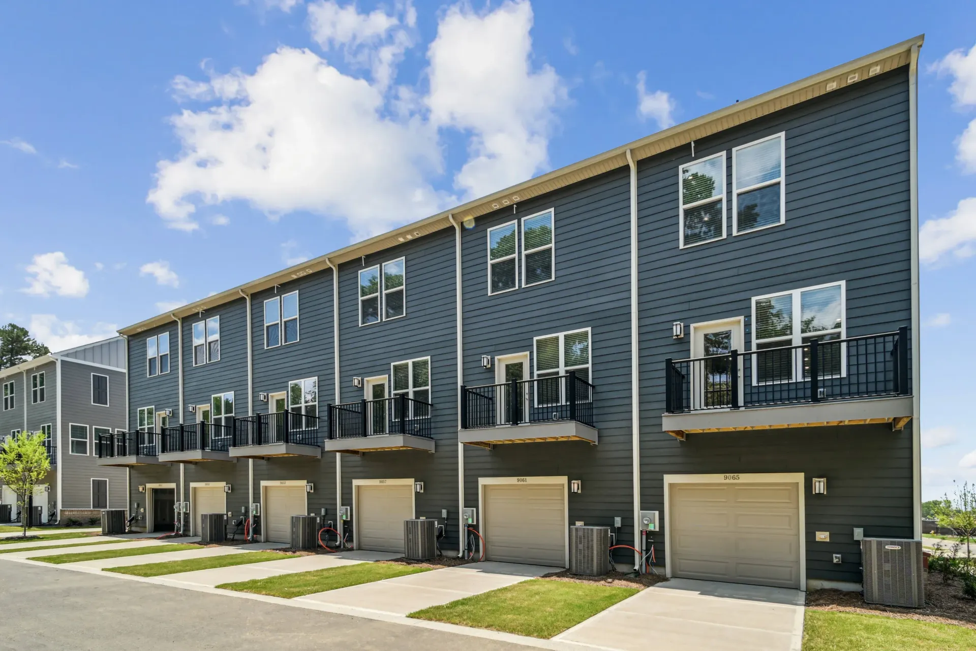 Row of modern townhouses with blue-gray siding, beige garage doors, and small balconies under a cloudy sky.