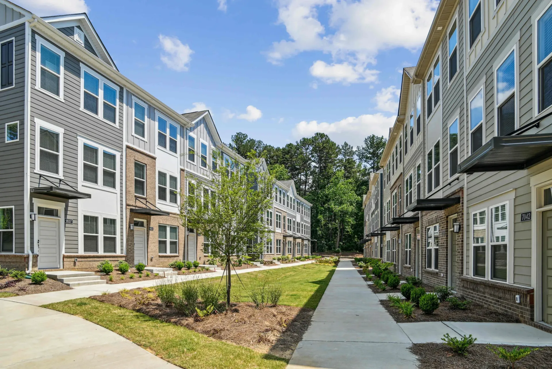 Rows of townhomes with gray siding, blue sky, and green lawn.