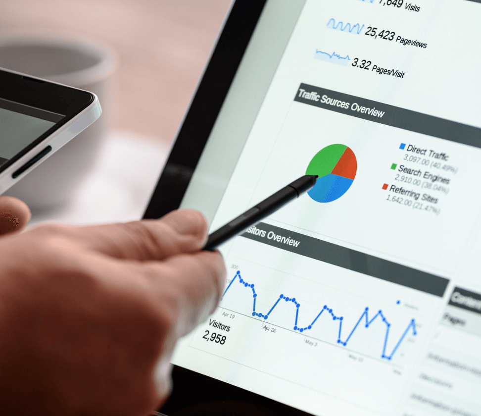 Hand holding stylus pointing at tablet dashboard with pie chart and line graph