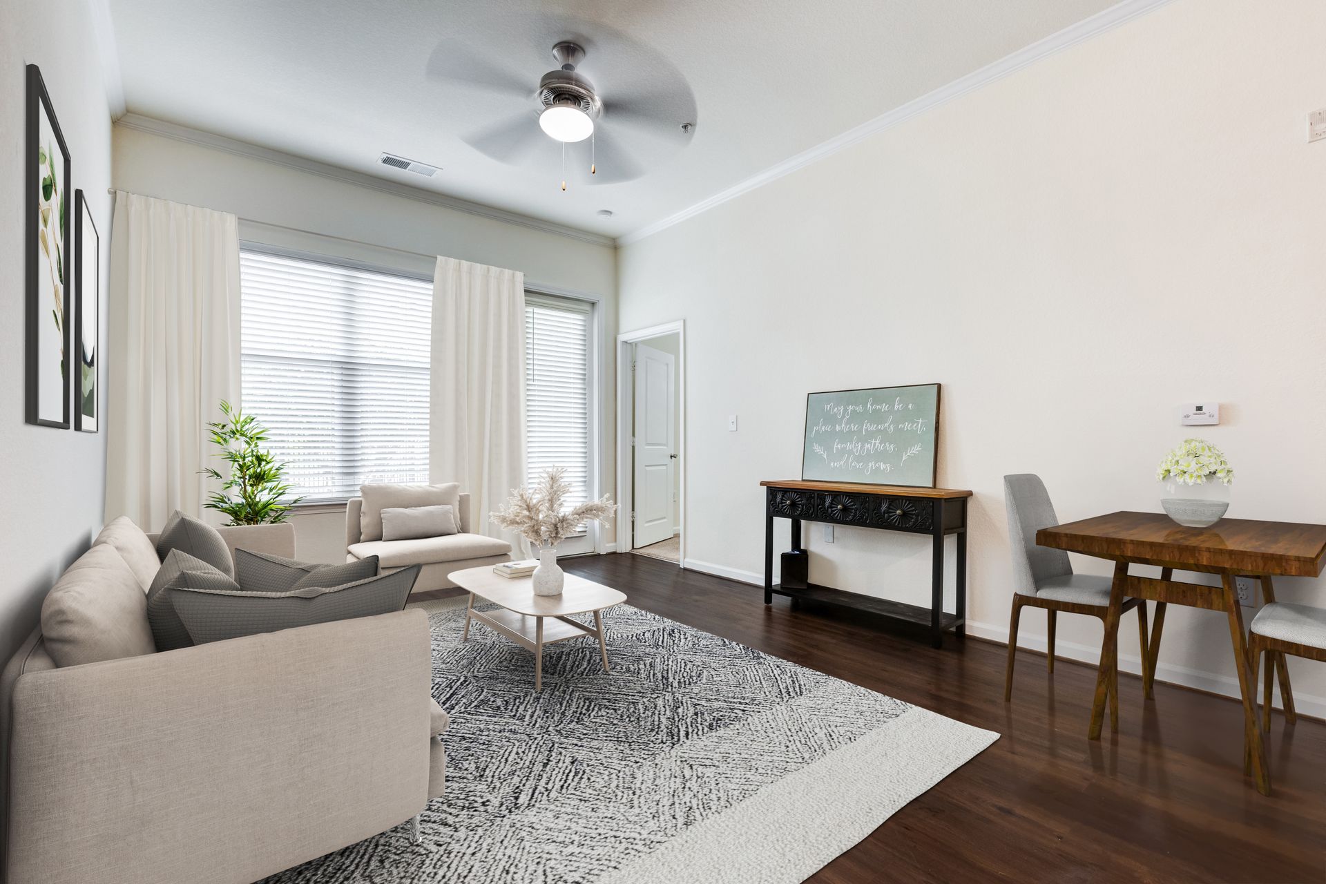 Living room with light-colored sofa, rug, and dining table on dark wood floor, white walls, and curtains at Town Center at Lake Carolina in Columbia, SC.