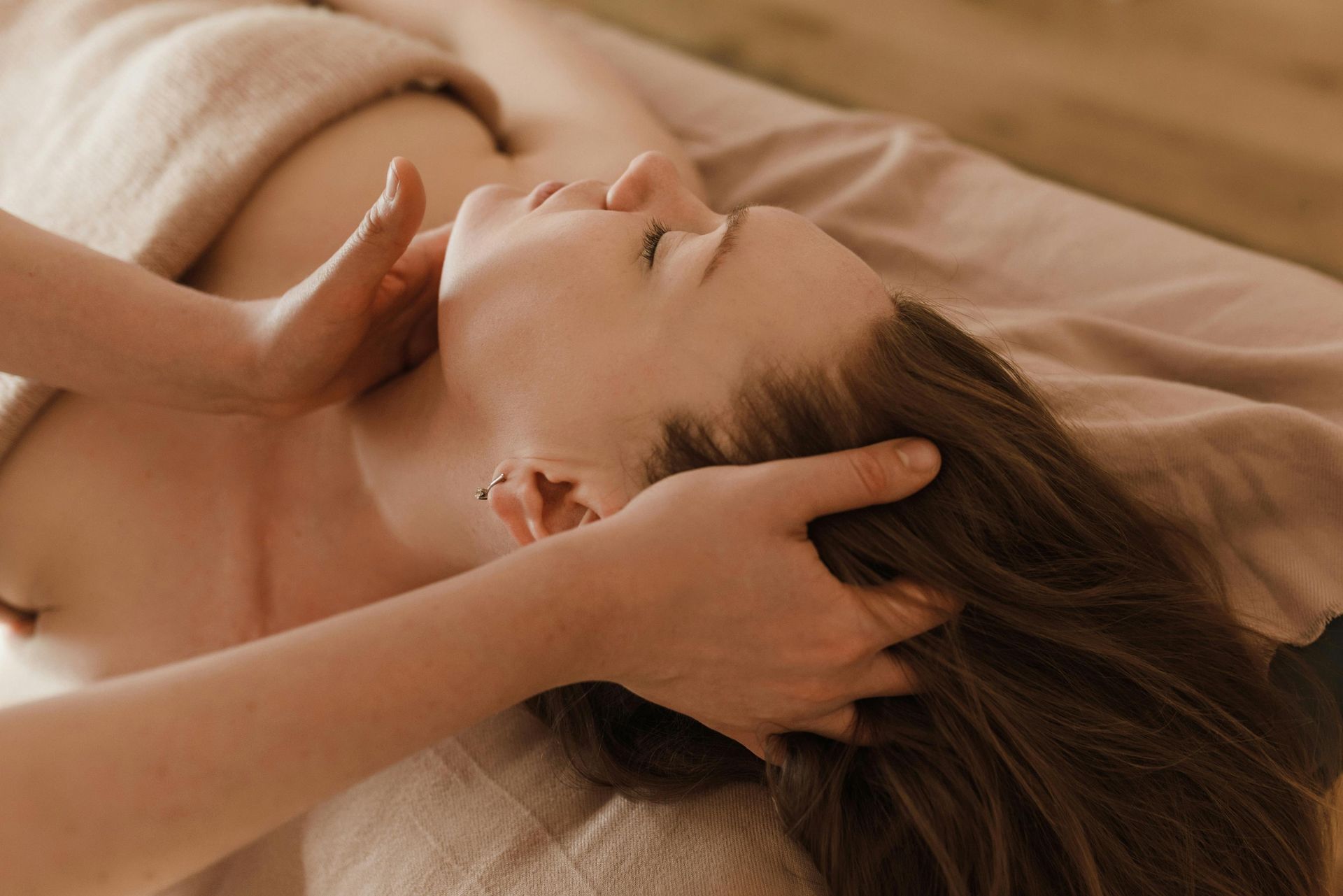 Woman receiving a head massage on a massage table; neutral tones.
