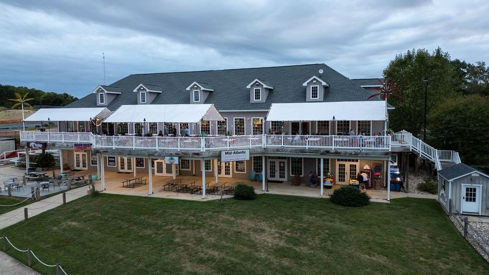 Large white beachfront hotel with balconies and a gray roof on a grassy hill under cloudy skies