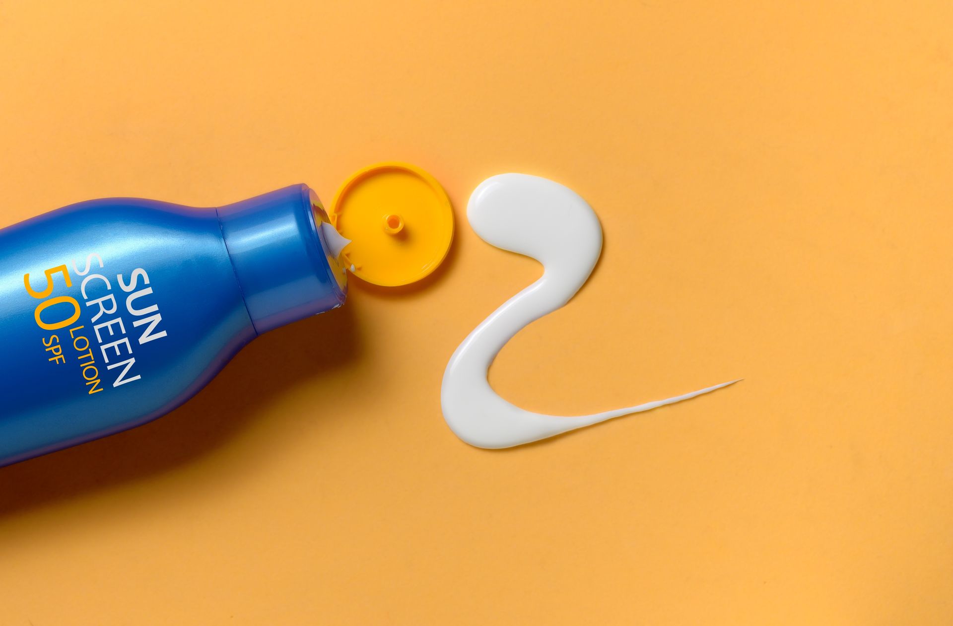 Blue sunscreen bottle with yellow cap and white lotion blob on orange background