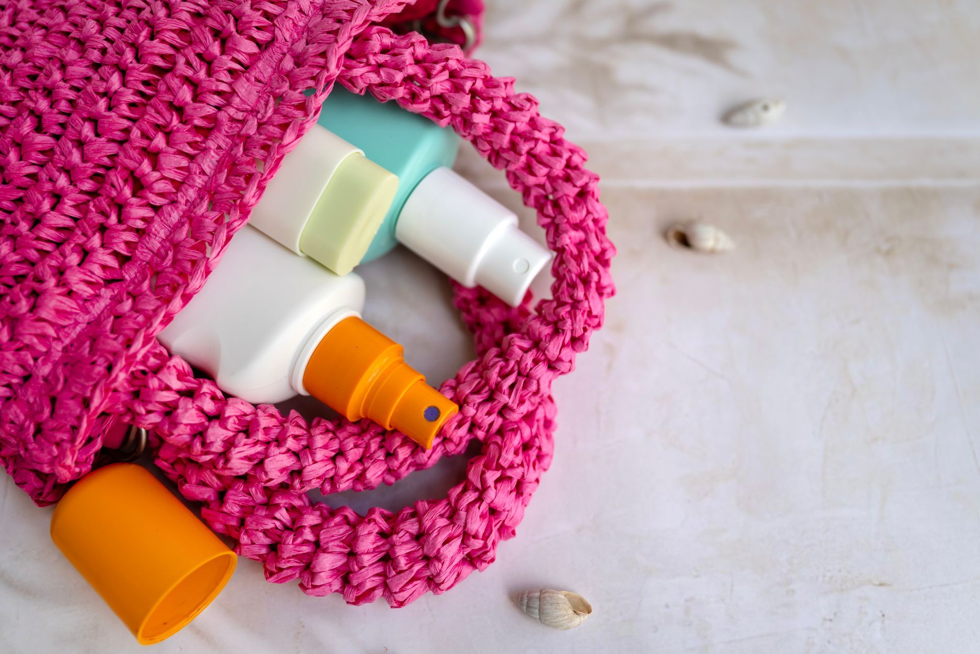 Pink crocheted bag holding sunscreen bottles on a light wooden surface