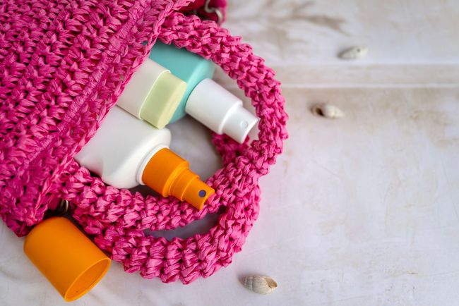 Pink crocheted bag holding sunscreen bottles on a light wooden surface