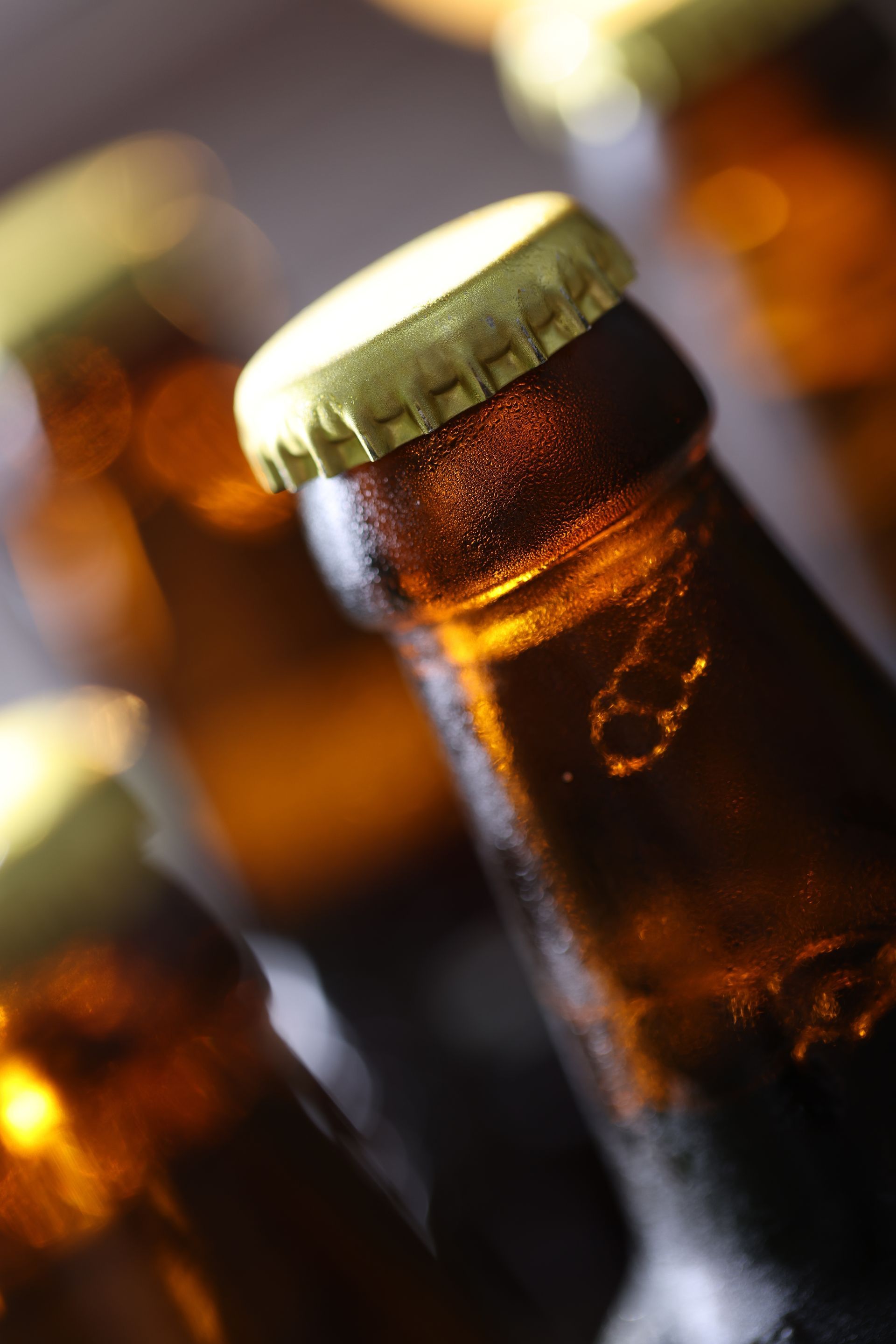 Close-up of amber glass beer bottles with gold caps, softly lit and out of focus