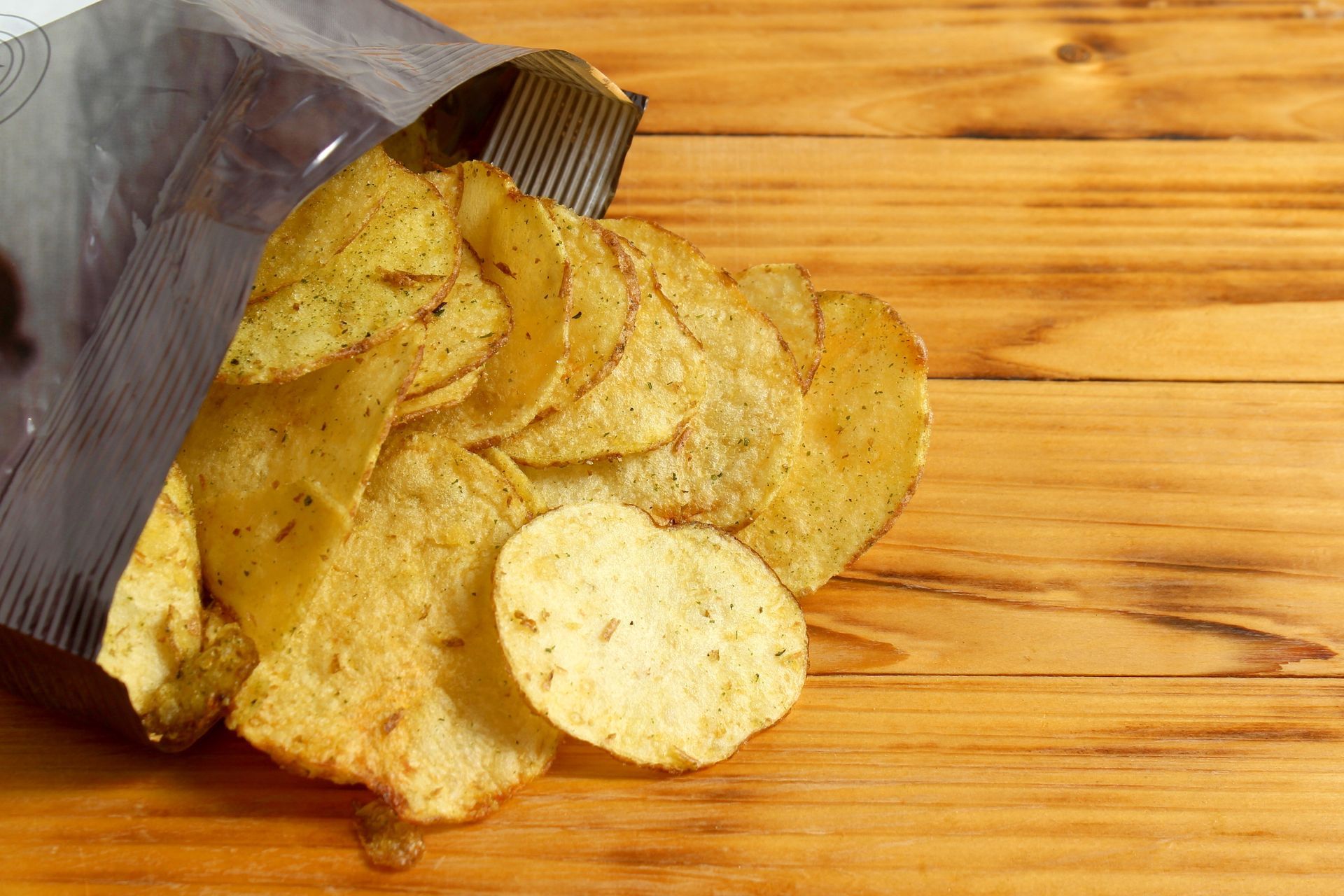 Potato chips spilling from a opened bag onto a wooden surface