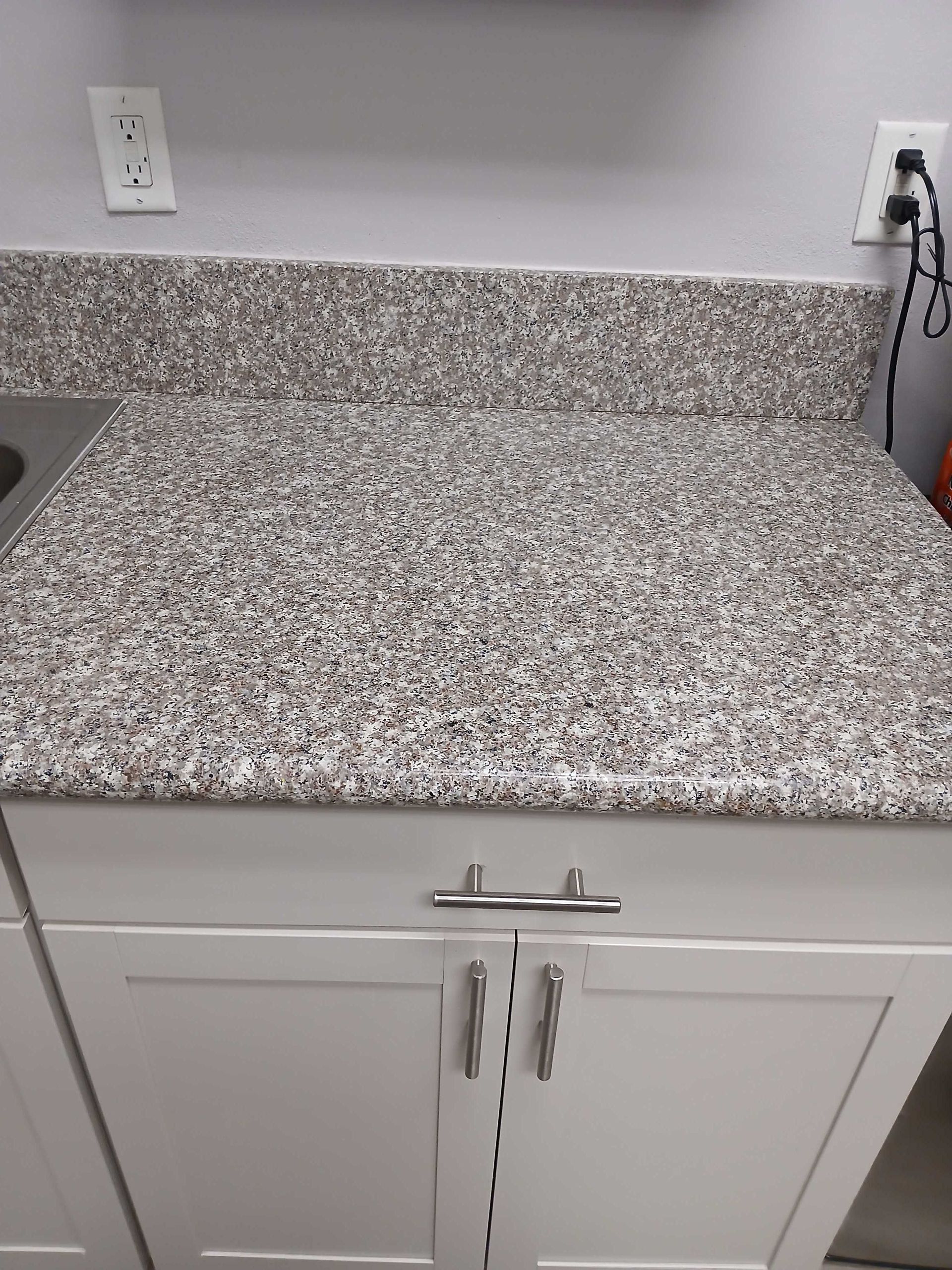 A kitchen counter with a granite counter top and white cabinets.