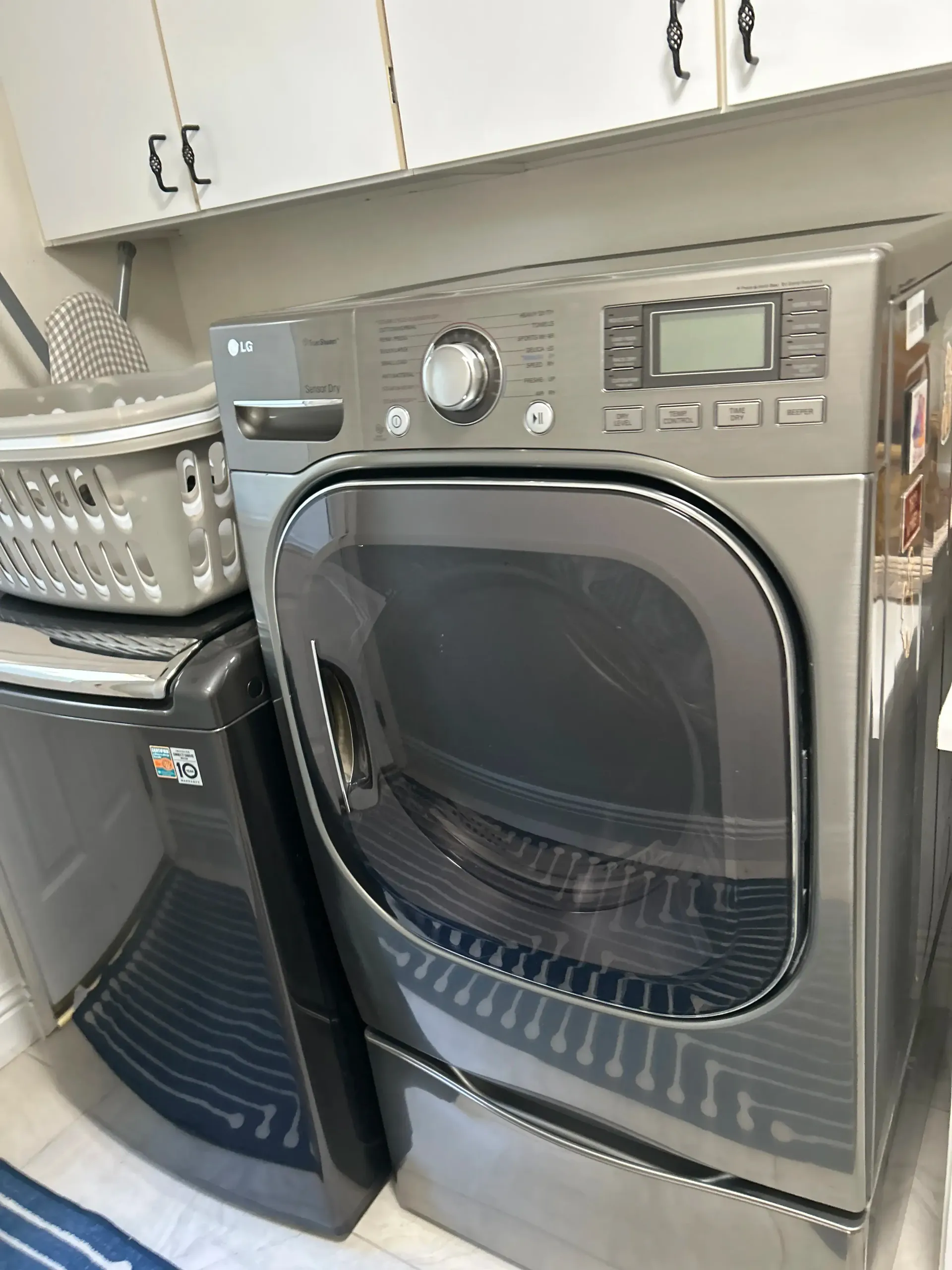 A stainless steel dryer is sitting next to a black washer and dryer in a laundry room.