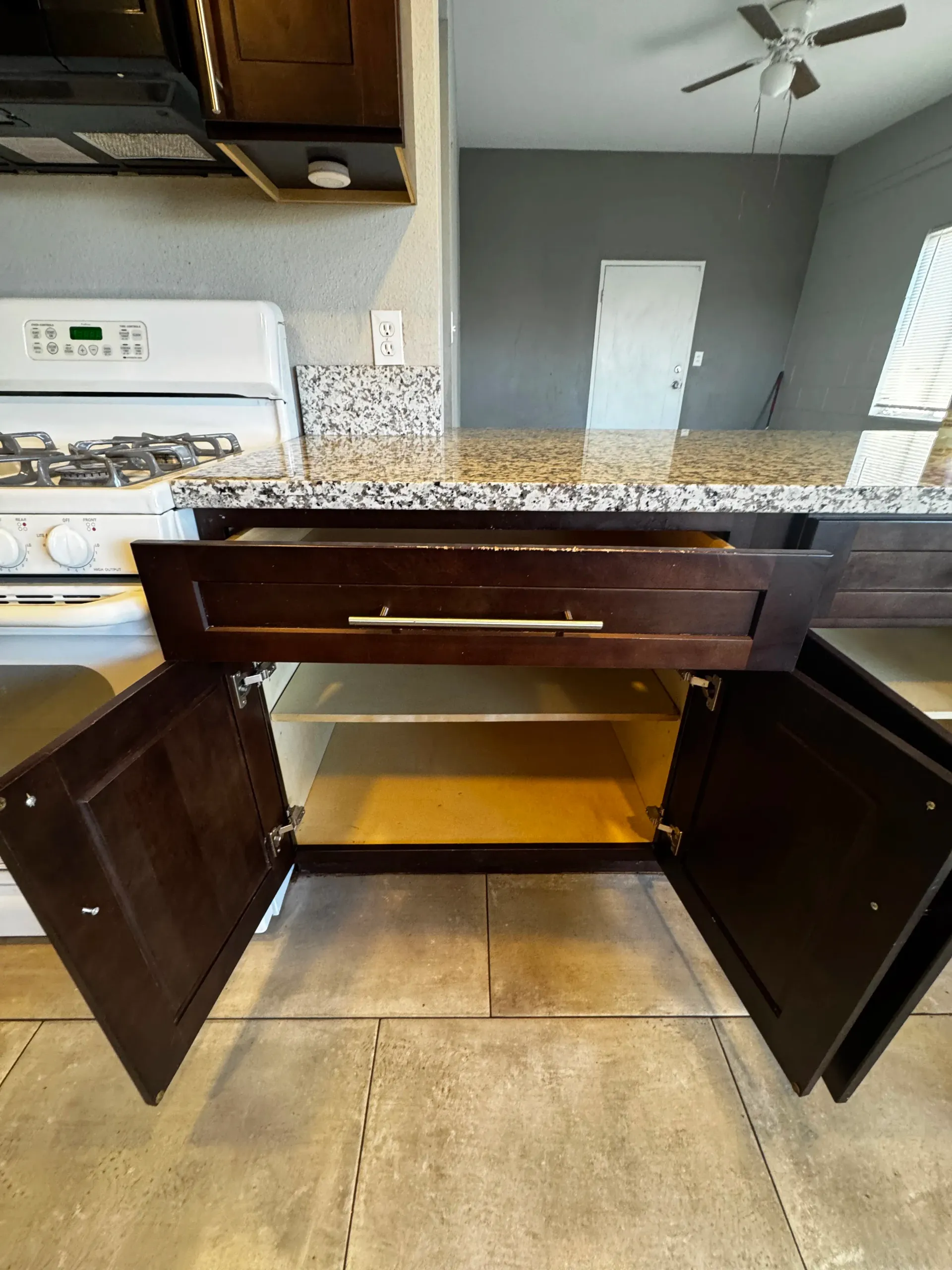 A kitchen with a stove , sink , and cabinets open.