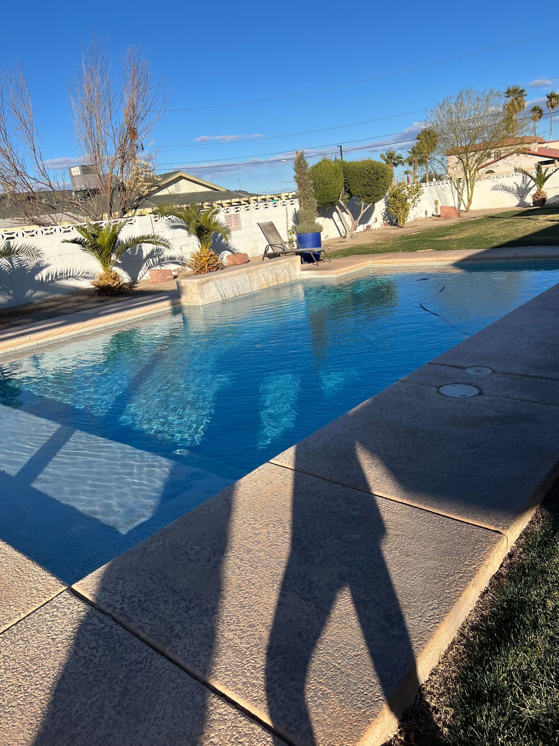 A shadow of a person is cast on the side of a swimming pool.