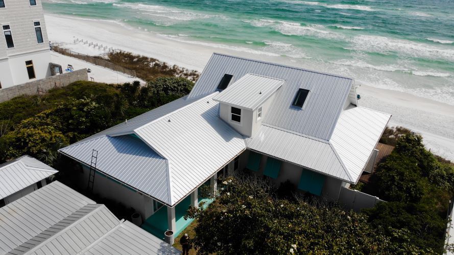 An aerial view of a white house on a beach next to the ocean.