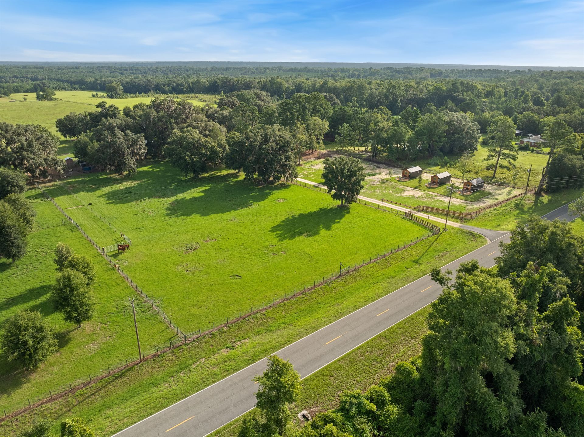 An aerial view of a lush green field surrounded by trees and a road.