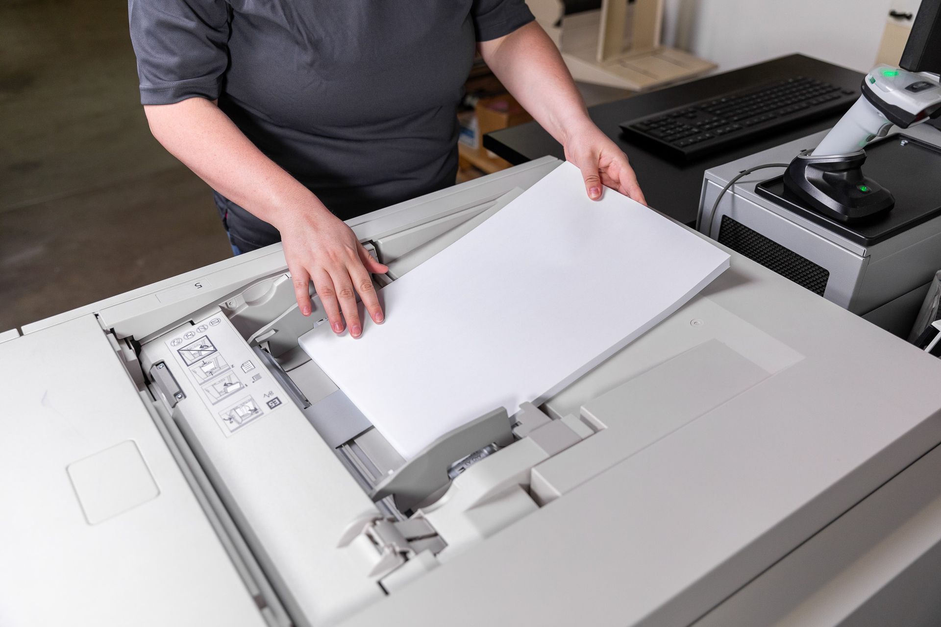 Person placing a stack of white paper into a gray copier.