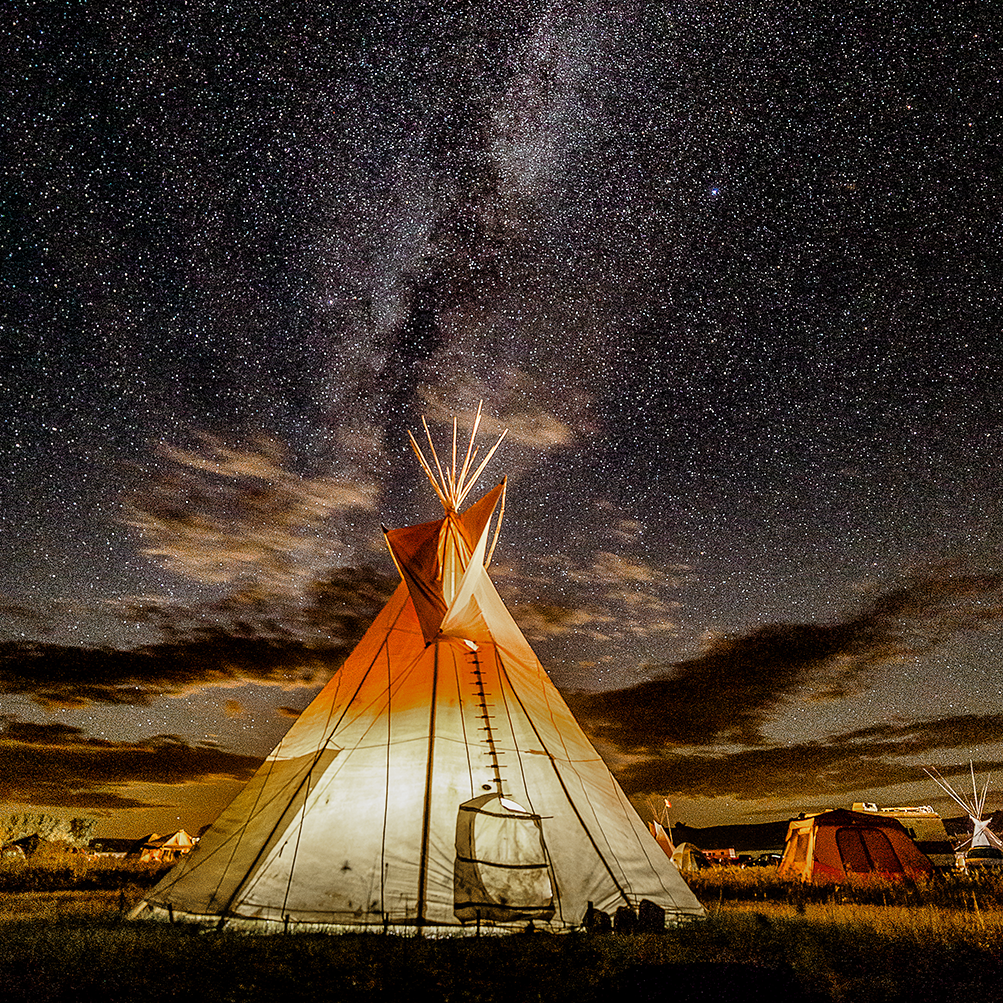 Teepee under a dark, starry night sky. The Milky Way is visible.