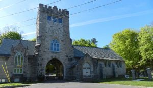 Stone building with a central archway, tower, and gray roof against a blue sky.