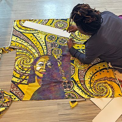 Artist assebling a large yellow, purple, and black quilt on the floor