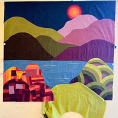 Colorful fabric landscape with layered hills, blue water, a glowing sun, and patterned trees under a purple sky