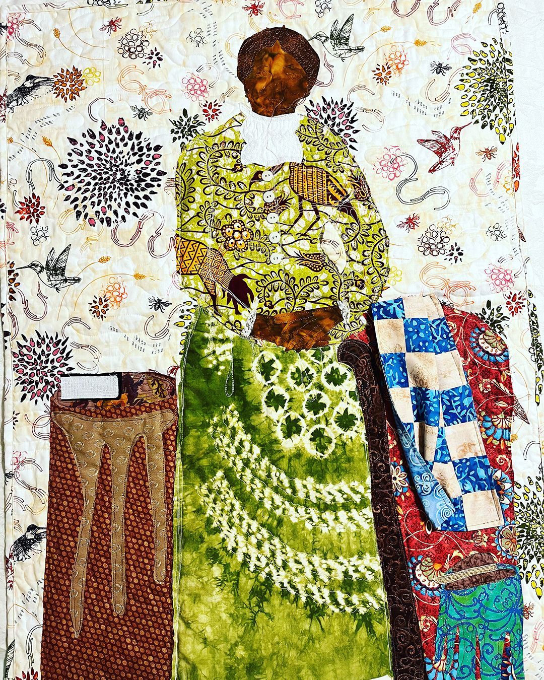 Person in a patterned dress stands beside textiles and hanging fabric swatches.