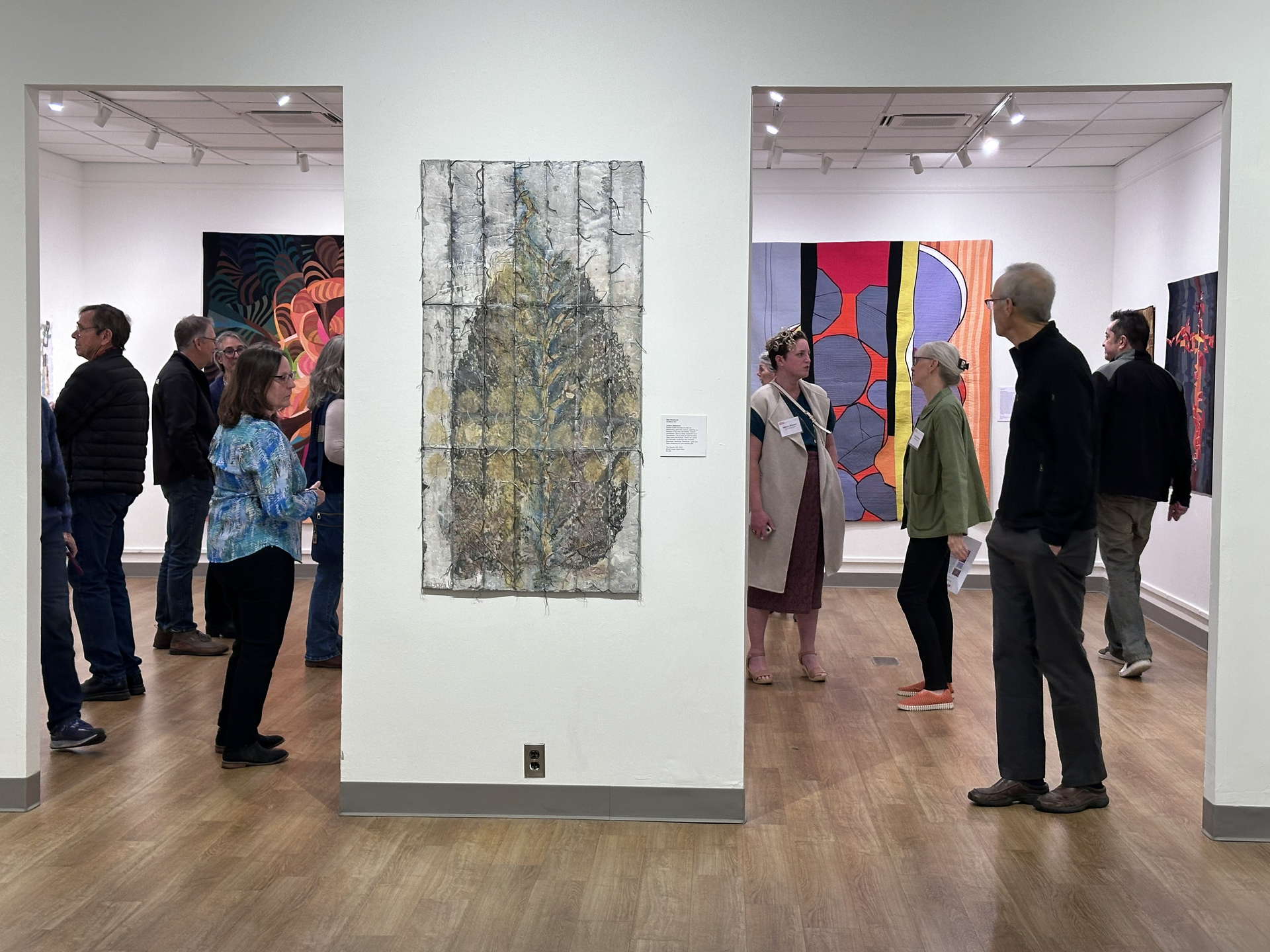 Art gallery with people viewing colorful abstract paintings in a white-walled exhibition space