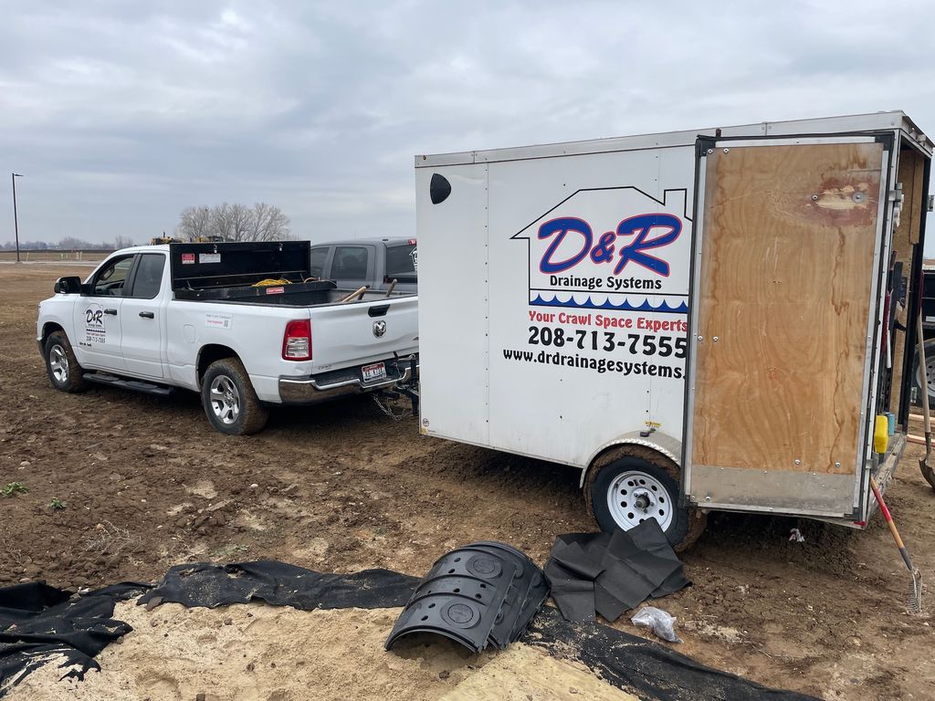 White pickup beside a damaged white trailer on muddy ground, with debris scattered nearby.