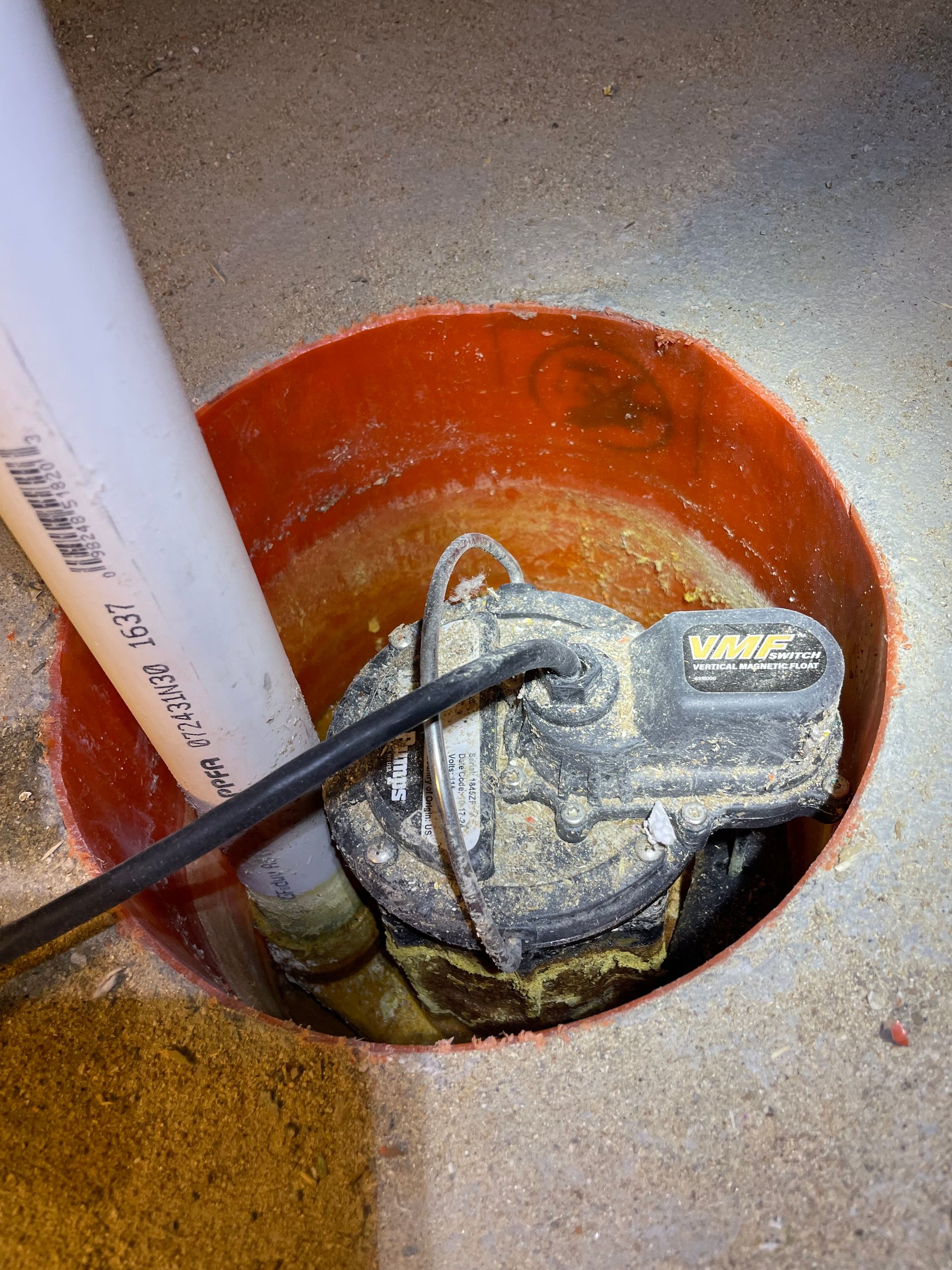 Water pump with black hose in a red utility pit, viewed from above.