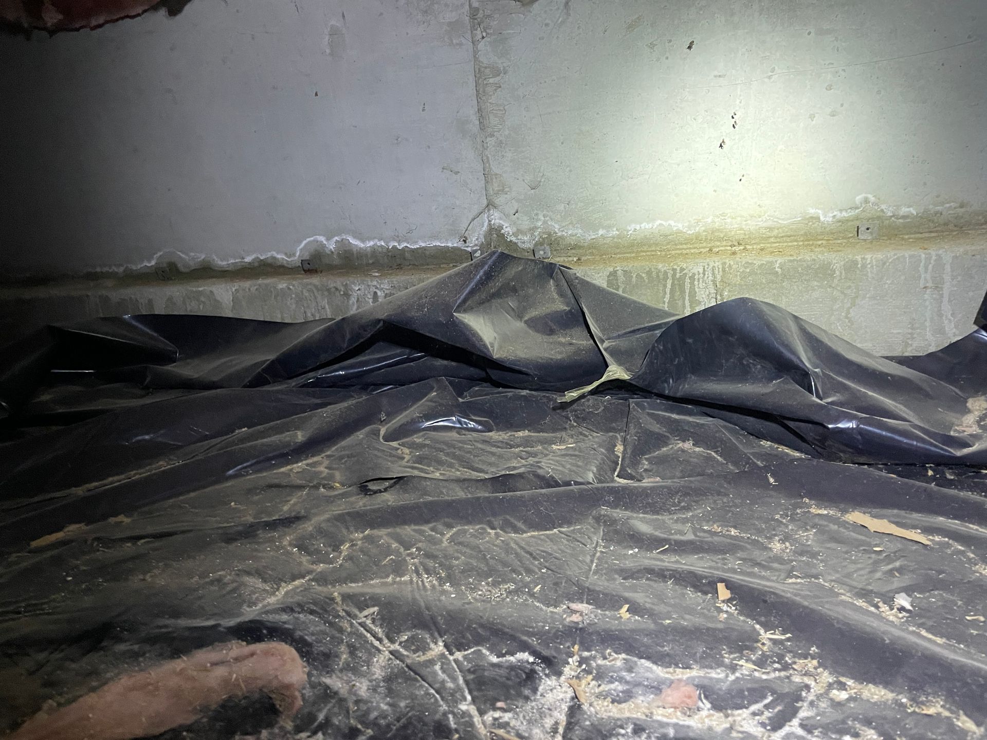 Black tarp and debris along a cracked wall, with a hand visible in the lower left corner.