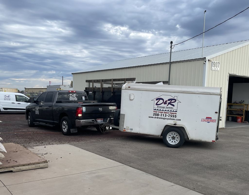 Black pickup truck towing a white enclosed trailer in an industrial parking lot under cloudy skies