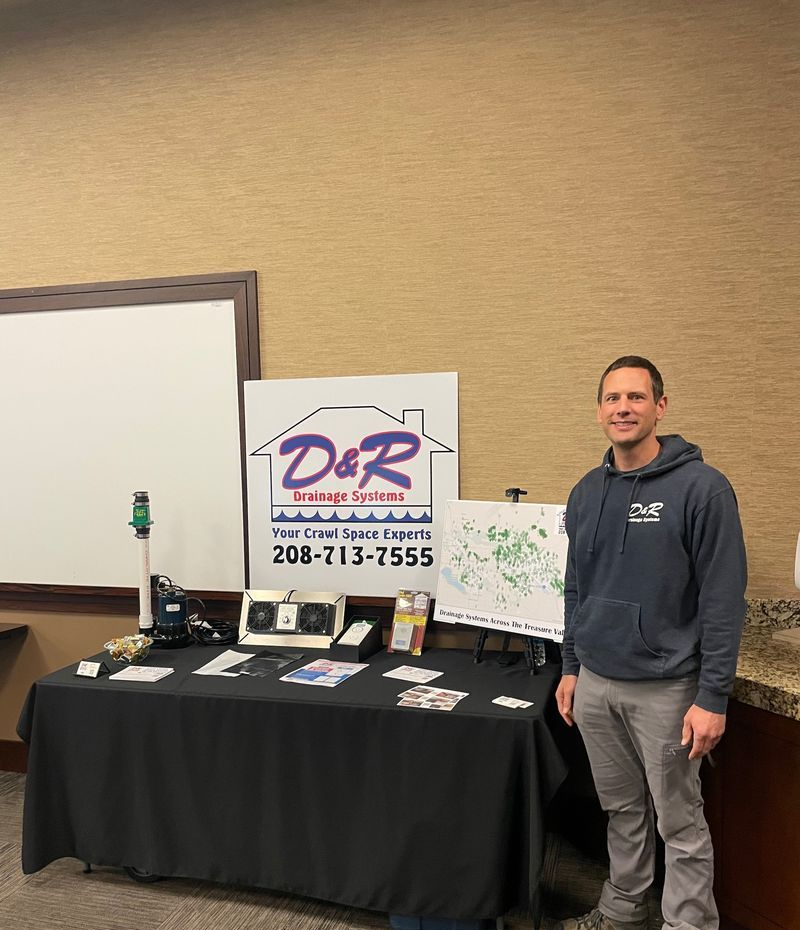 Trade show booth with a D&R Services sign, brochures, and a man standing beside the display.
