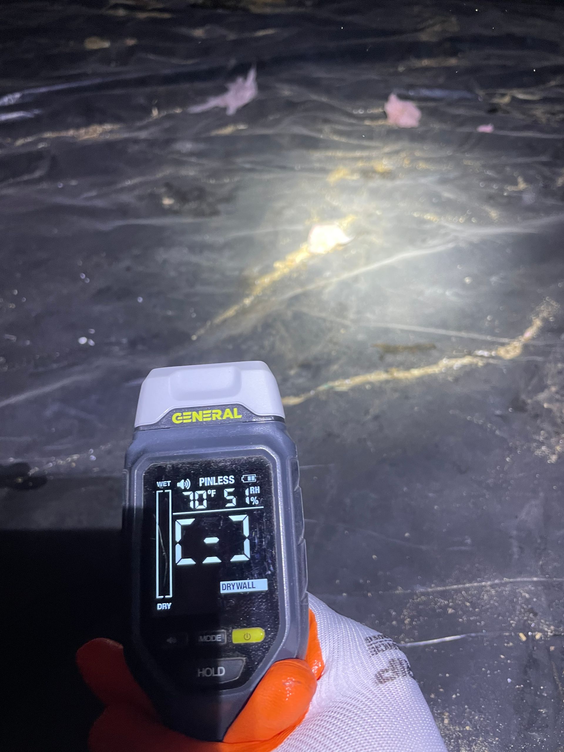 Handheld infrared thermometer aimed at dark icy ground with a bright reflective spot.