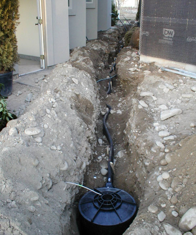 Construction trench with black pipe and utility box beside a building