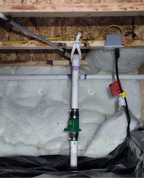 White pipe assembly with green valve and insulated wall cavity, with cables and a small electrical box above.