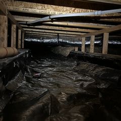 A low-angle view inside a crawlspace showing wooden floor joists, black plastic vapor barrier, and insulated ductwork.