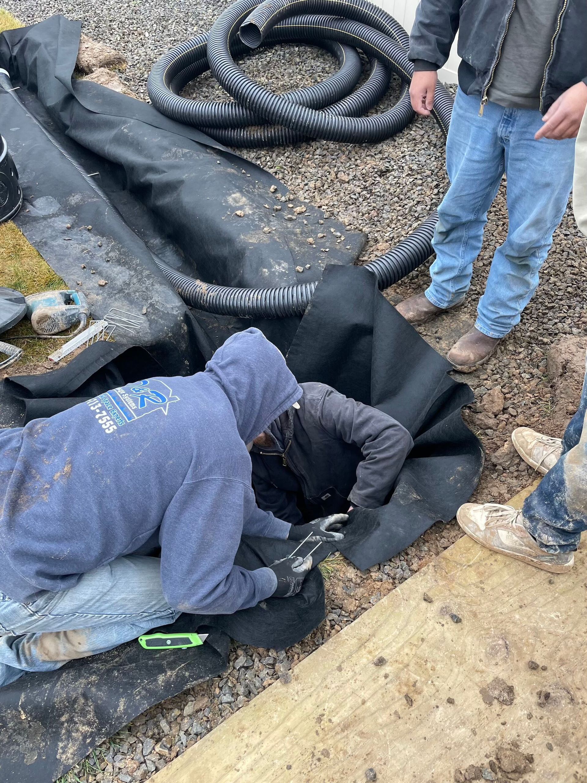 Workers installing black pond liner in a gravel-lined pit