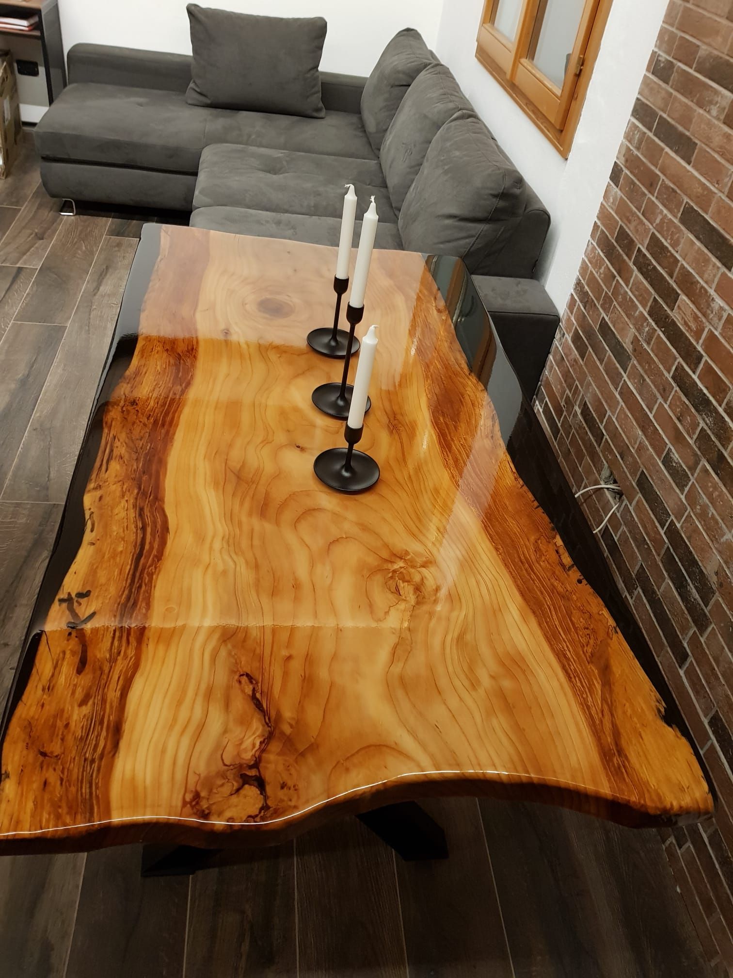 Tavolino da caffè in legno con resina epossidica e candele; divano componibile grigio sullo sfondo.