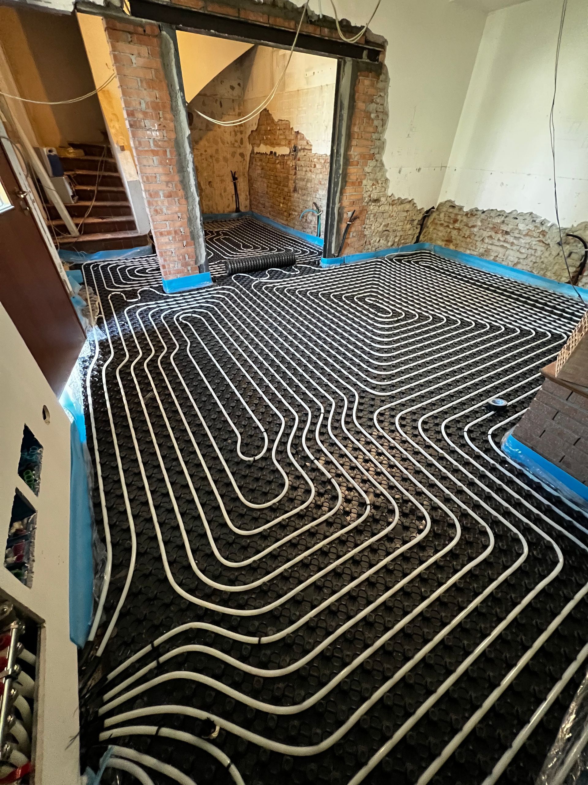 Installazione di riscaldamento a pavimento; materassino isolante nero con tubi bianchi stesi in una stanza in costruzione.