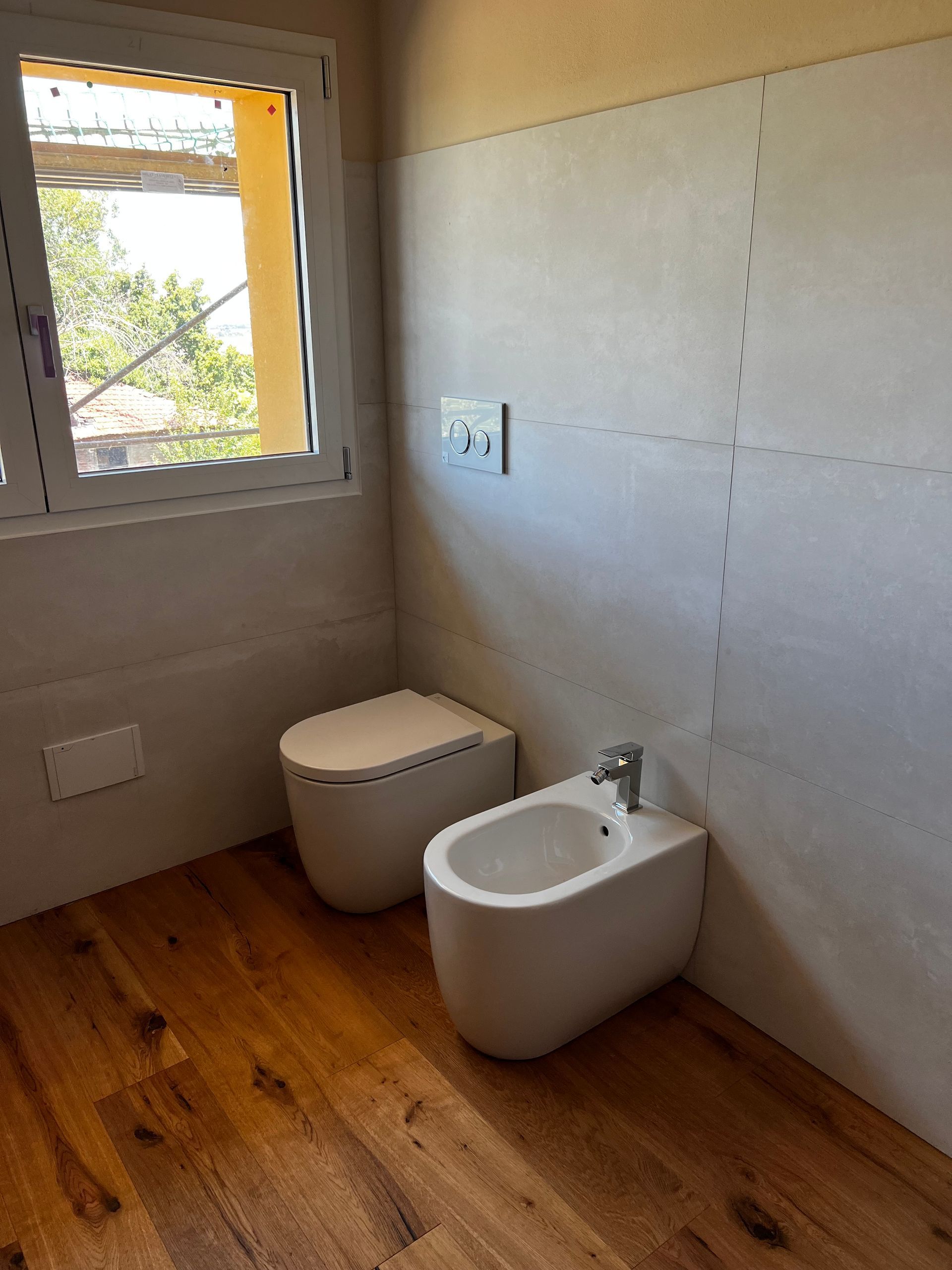 Bagno con WC e bidet moderni, pavimento in legno e finestra.