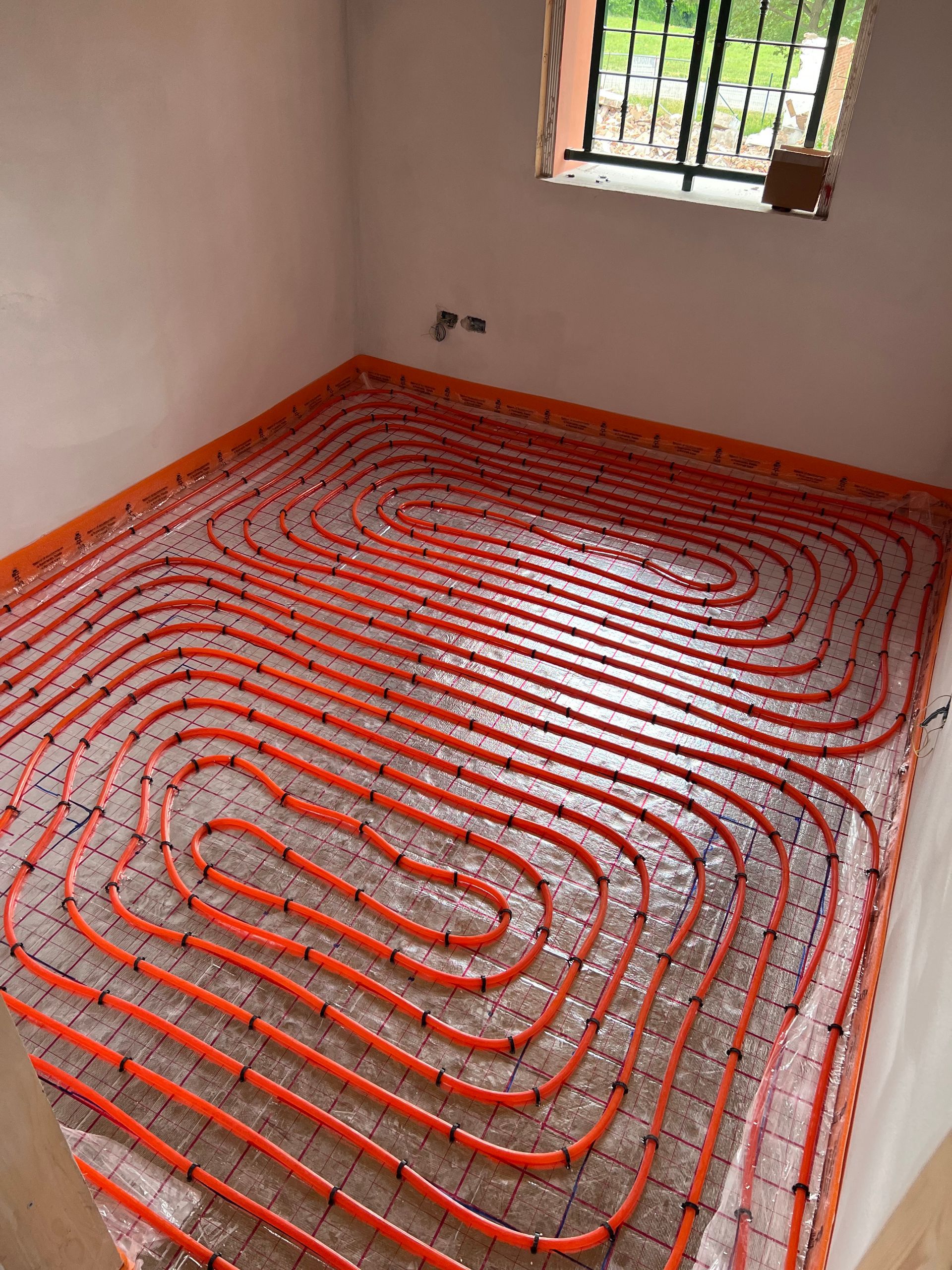 Tubi di riscaldamento a pavimento radiante arancioni installati in una stanza, pronti per il calcestruzzo.
