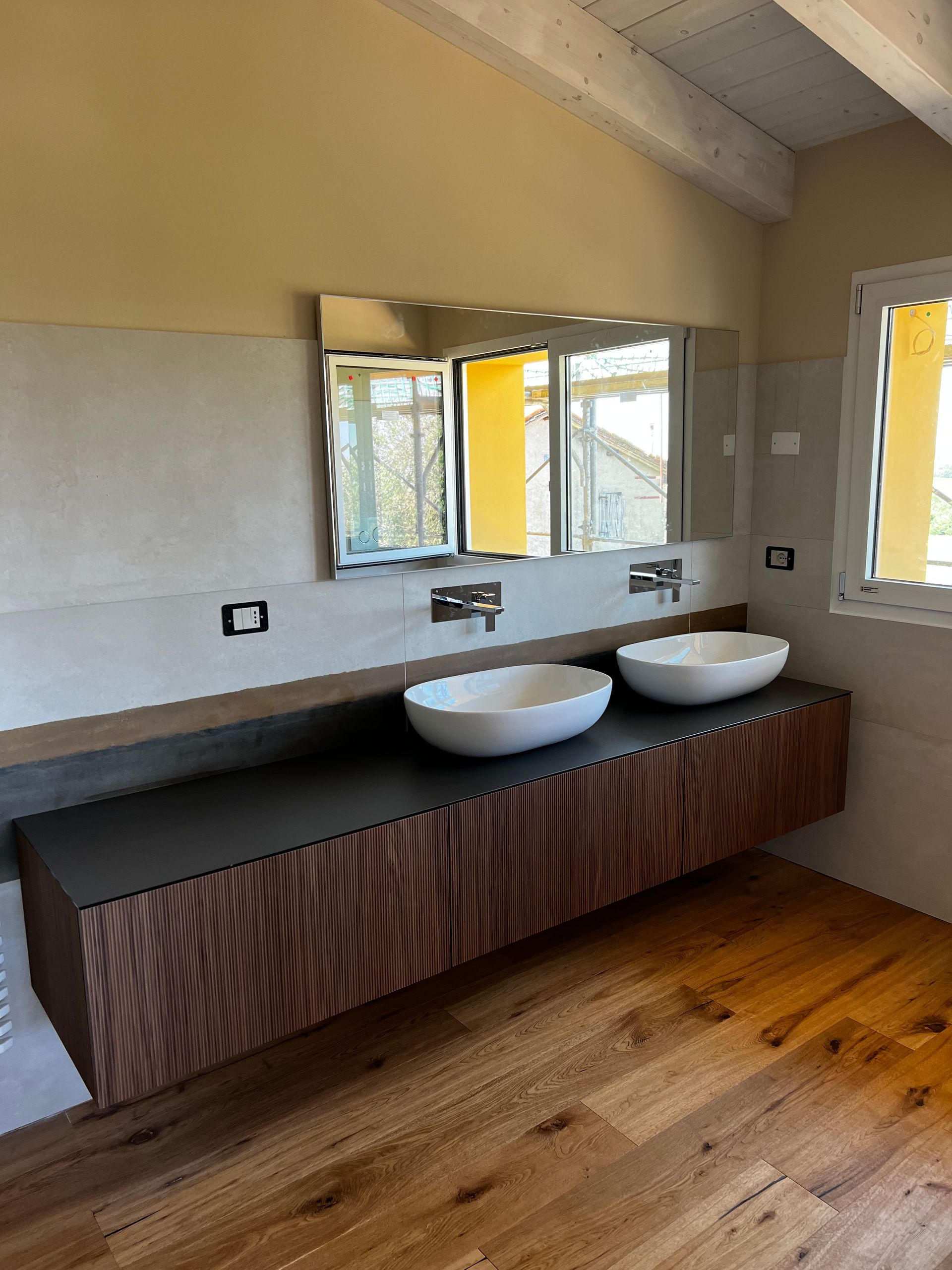 Bagno con mobile lavabo sospeso in legno, lavandini bianchi, specchio e pavimento in legno.